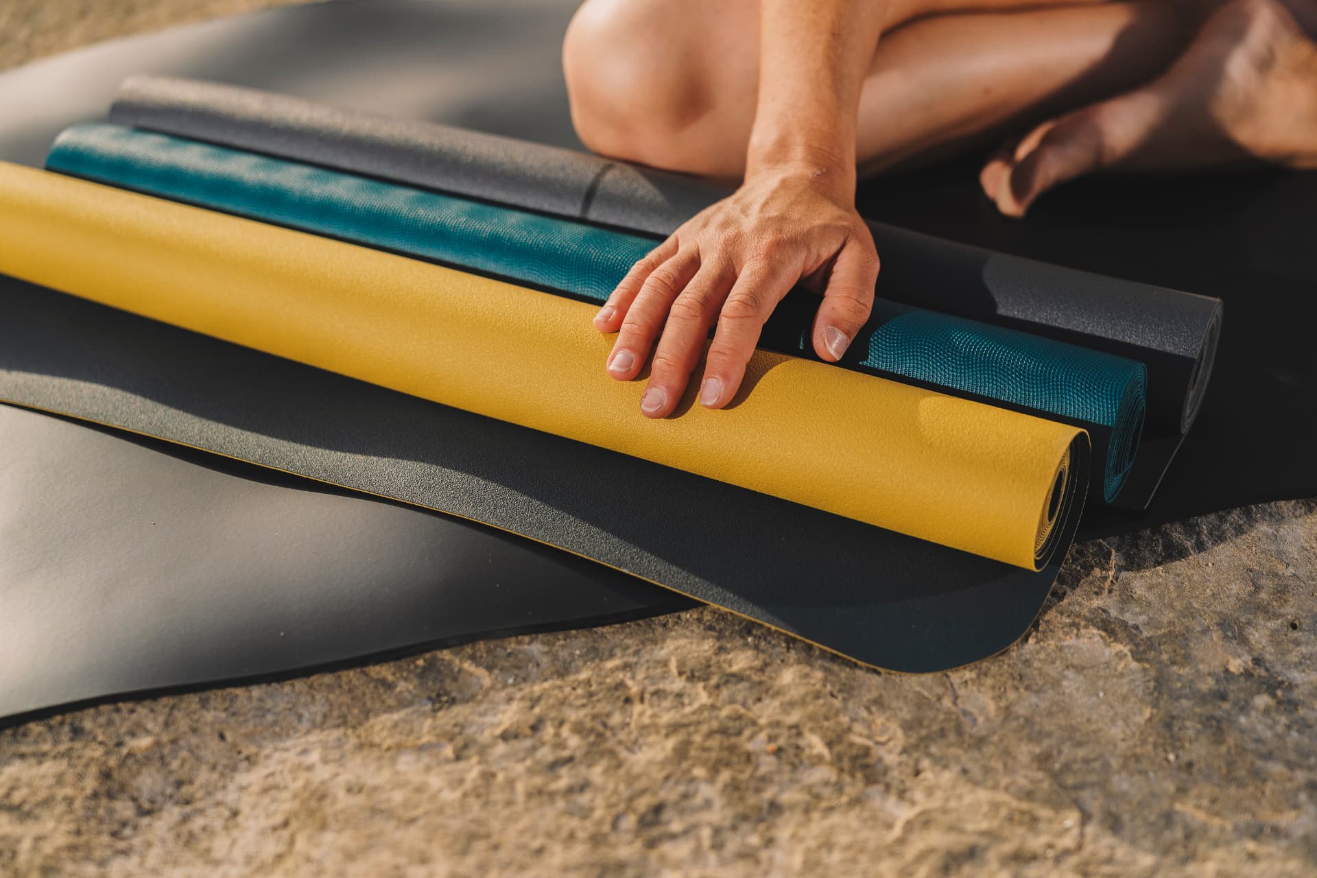 Rolled yoga mats in yellow, teal and grey foam on a sunlit stone floor